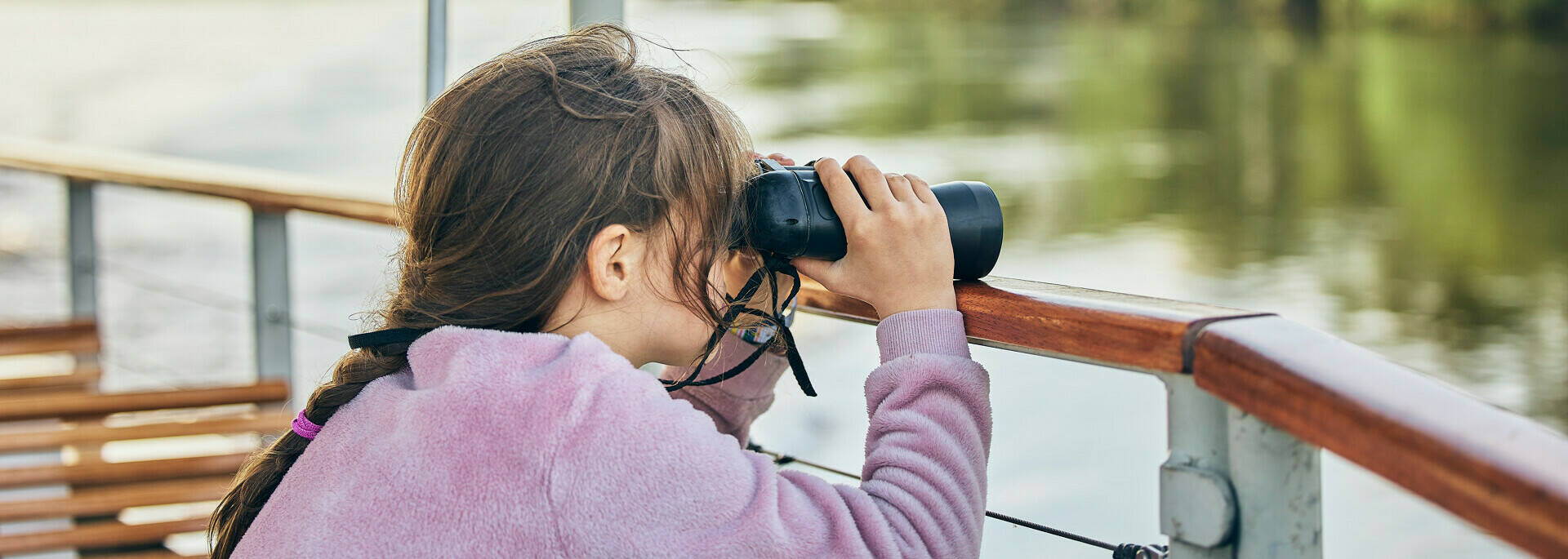 Girl observing the banks of the Loire from the boat with binoculars