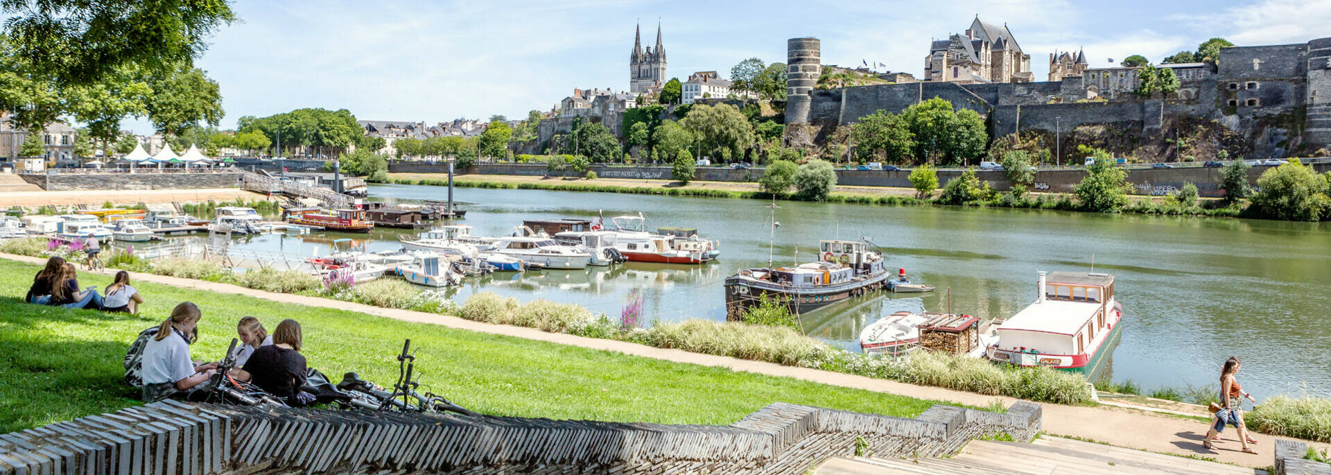 Jóvenes sentados en la hierba cerca del puerto de Savatte, frente al río Maine y el castillo de Angers.