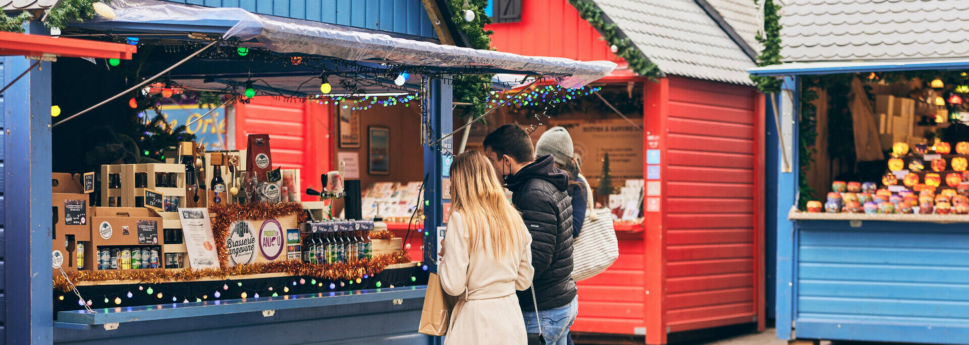 Un couple se baladant au marché de Noël d'Angers place du Ralliement, devant un chalet proposant des bières locales artisanales
