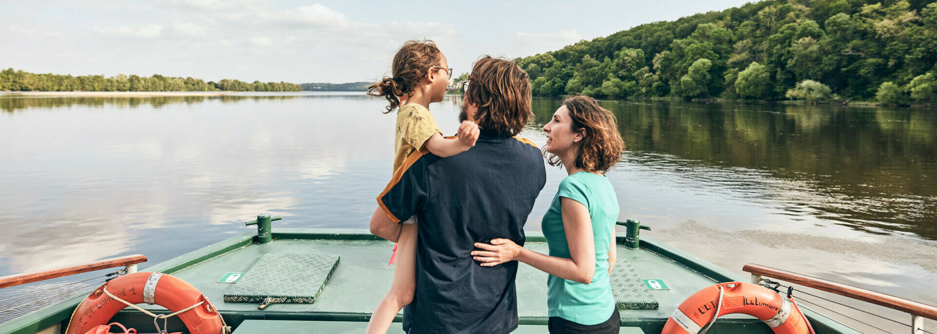 Un couple, dont l'homme porte une fillette, à l'avant du bateau face au fleuve