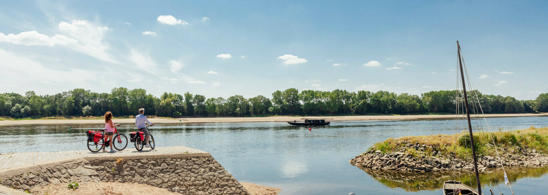 Couple à vélo arrêté au bord du fleuve pour regarder une gabarre passer