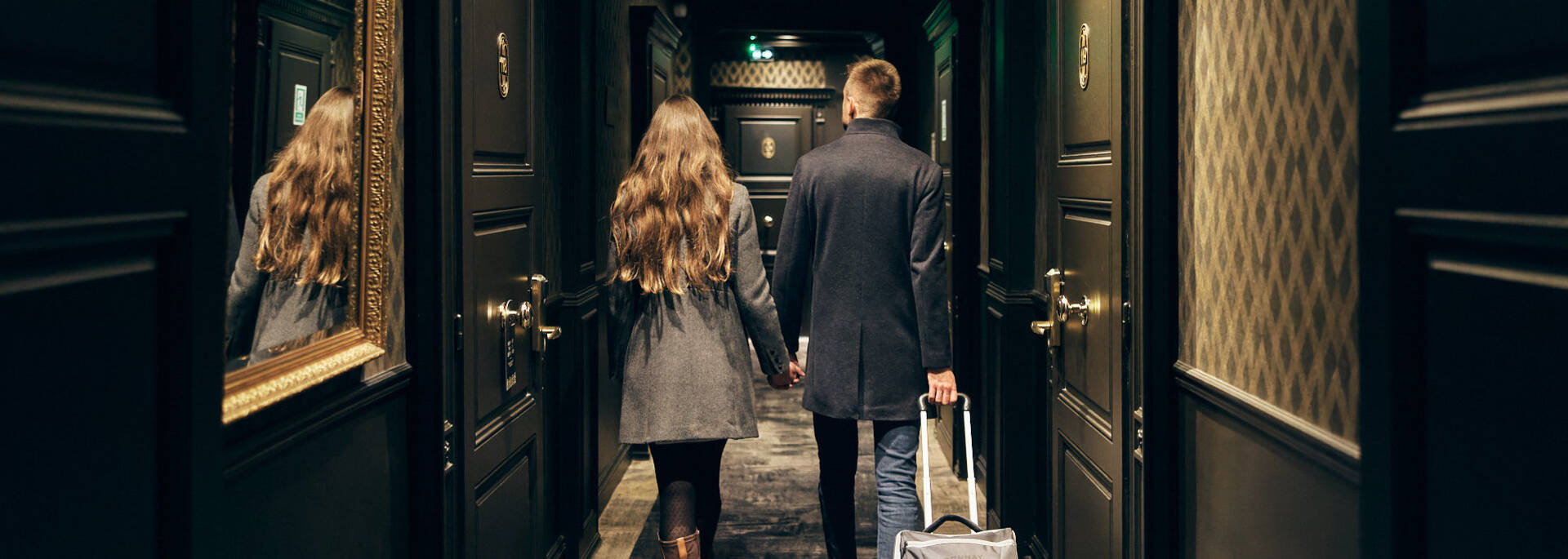 Couple en manteaux, marchant dans le couloir sombre de l'hôtel avec une valise