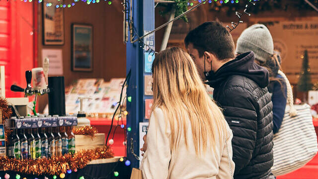 Un couple se baladant au marché de Noël d'Angers place du Ralliement, devant un chalet proposant des bières locales artisanales