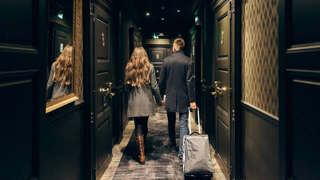 Couple en manteaux, marchant dans le couloir sombre de l'hôtel avec une valise