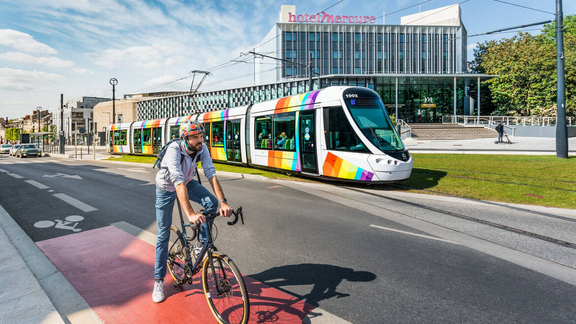 Homme à vélo avec le tram passant derrière, devant le Centre de Congrès d'Angers