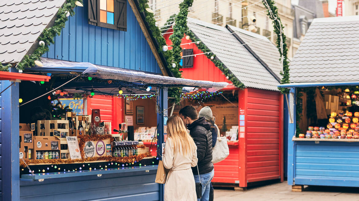 Un couple se baladant au marché de Noël d'Angers place du Ralliement, devant un chalet proposant des bières locales artisanales