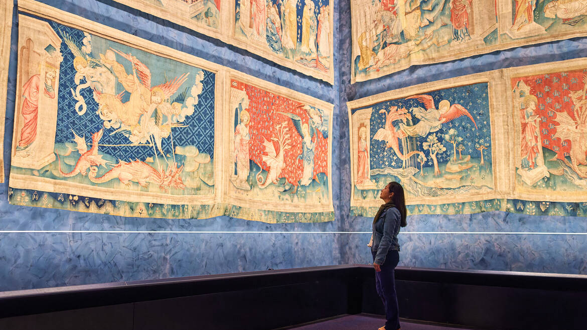 Une jeune femme regarde la Tenture de l'Apocalypse, inscrite au Registre Mémoire du Monde de l'UNESCO