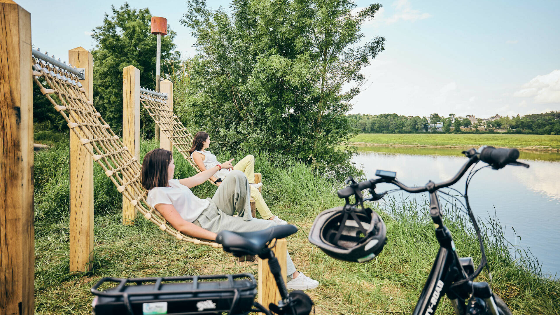 Deux jeunes femmes regardant la rivière, assises dans de grands hamacs, un vélo près d'elles