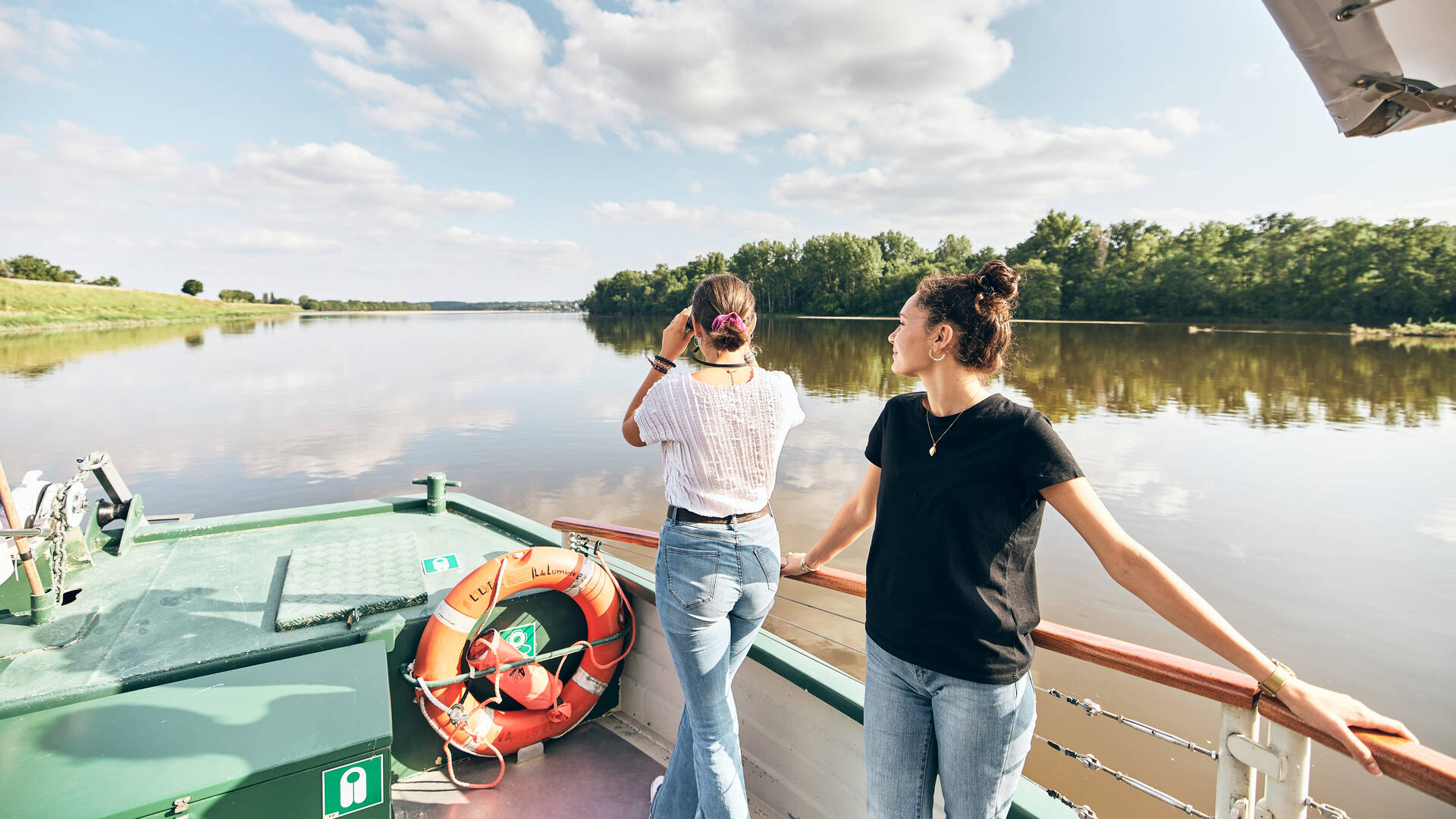 Two young women watching birds through binoculars from the front of a boat on the Loire