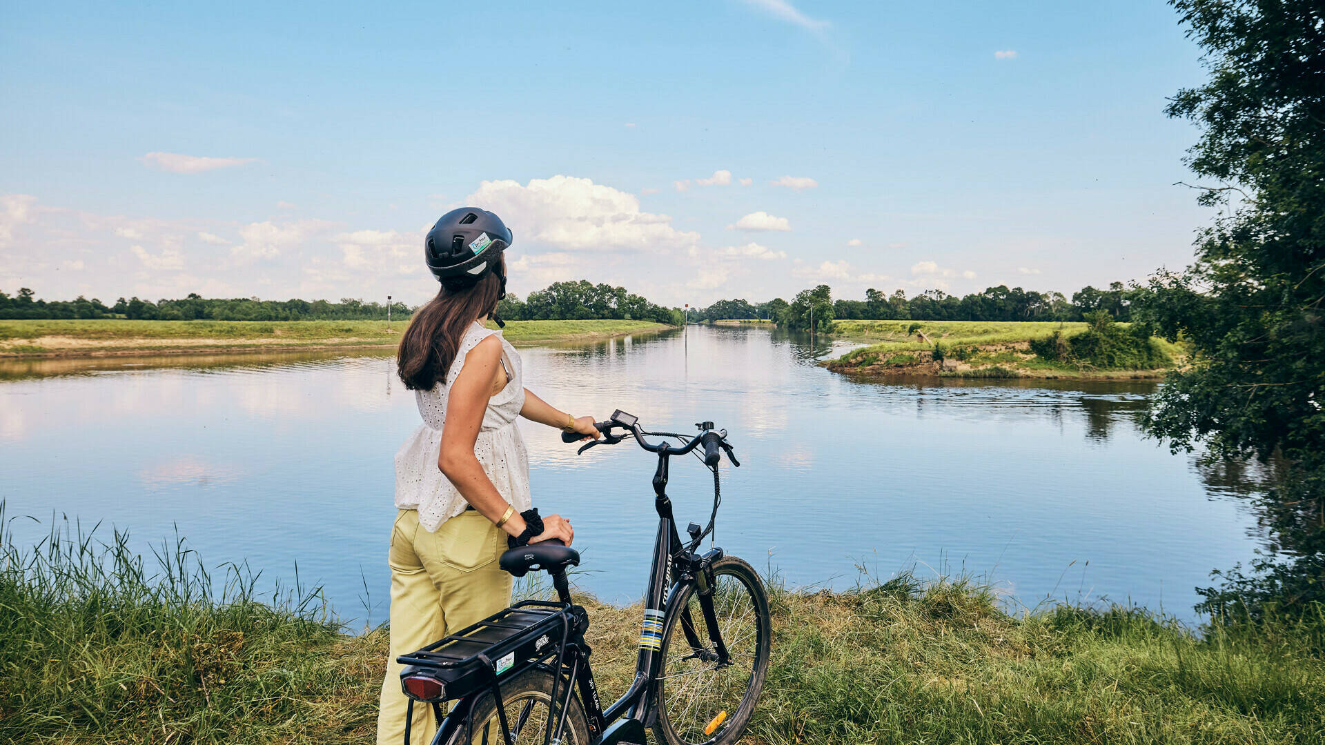 Young woman holding her bike in her hand on the river bank