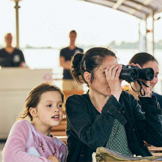 Une femme regardant dans les jumelles depuis le bateau, sa fille assise à ses côtés
